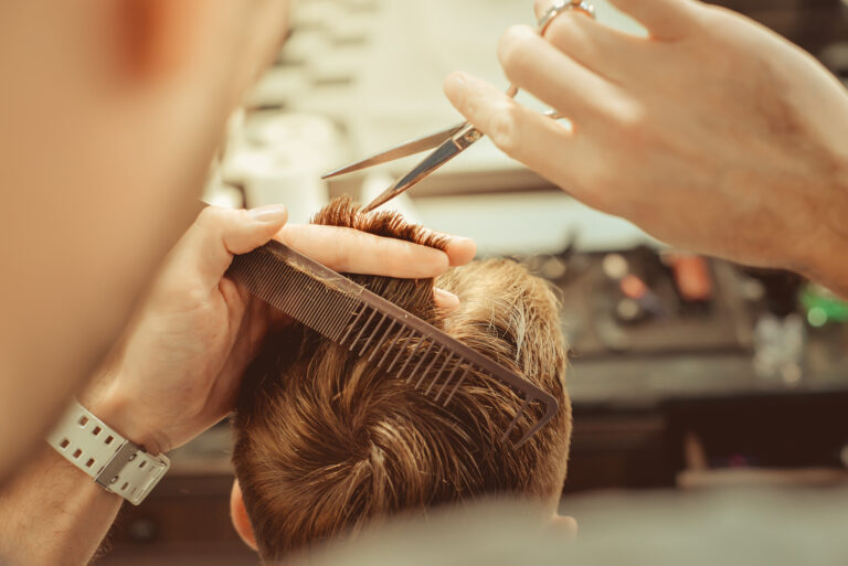 Barbershop. Close up of man haircut, master does the hair styling in barber shop. Toned vintage photos.